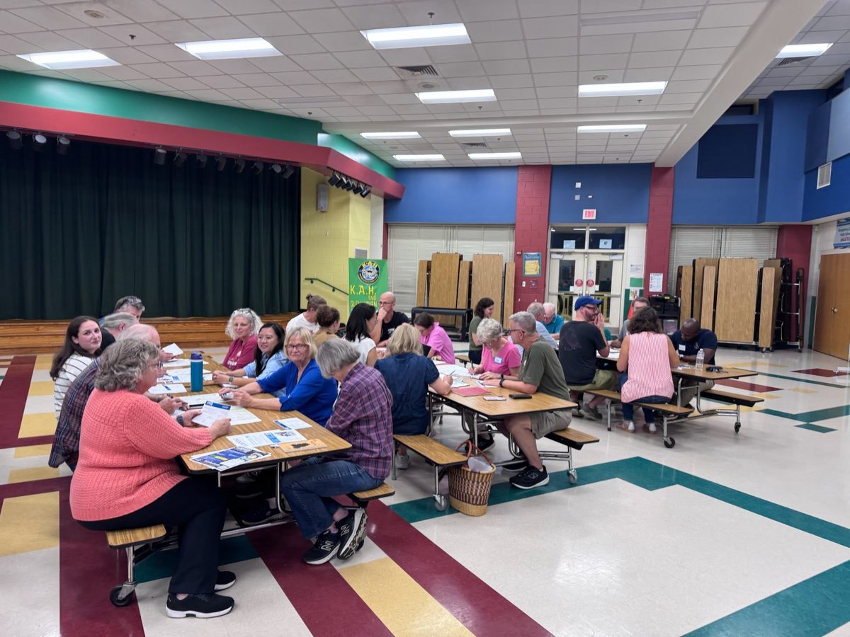 Neighbors seated at long cafeteria tables in the Glen Haven Elementary All Purpose Room, talking over Master Plan handouts.