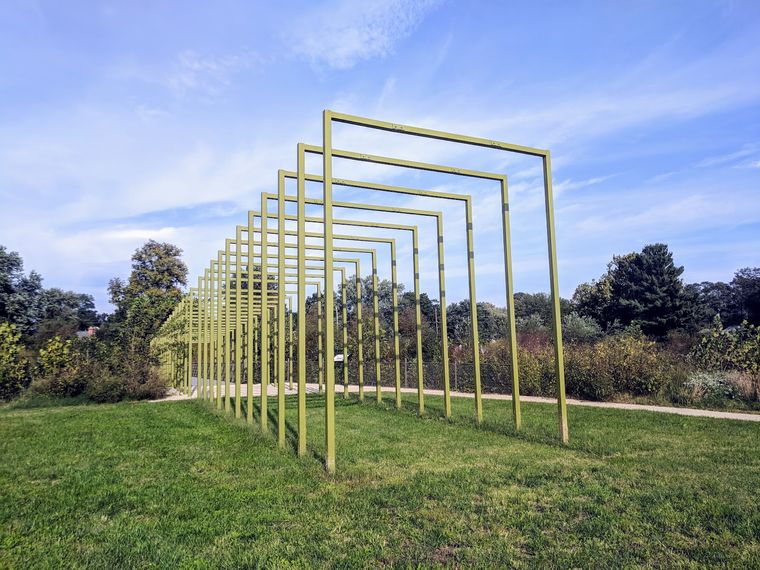 A row of yellow steel arches standing on the green under a blue sky