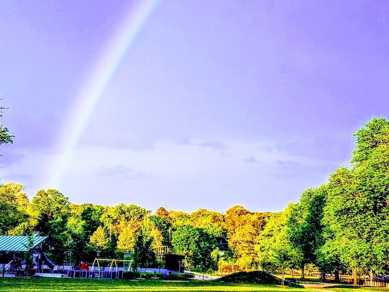 A rainbow arcing over the tree line above the park playground
