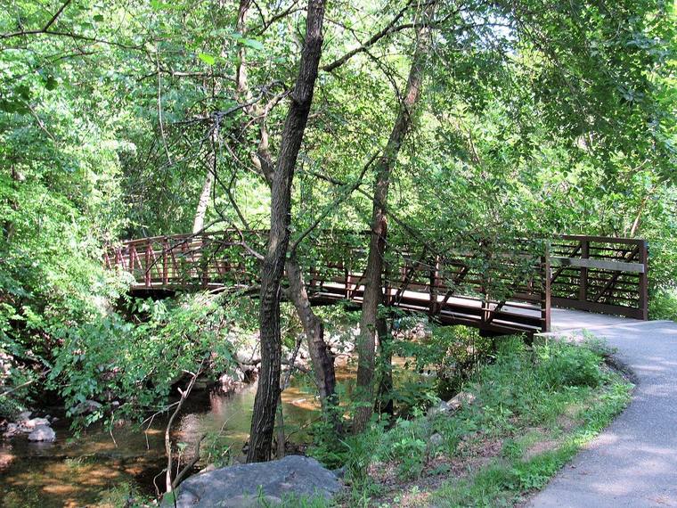 A wooden footbridge crossing Sligo Creek under green trees